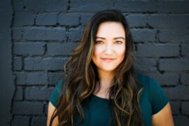 Woman with long brown hair posing in front of blue wall