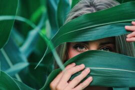 woman peeking through large leaves